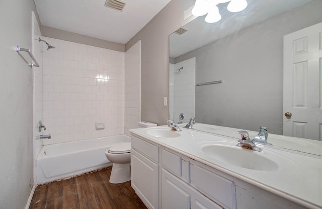 full bathroom with wood-type flooring, a textured ceiling, tiled shower / bath combo, vanity, and toilet