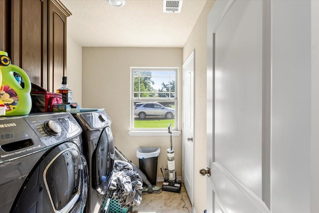 laundry area with washing machine and dryer, light tile patterned floors, cabinets, and a textured ceiling