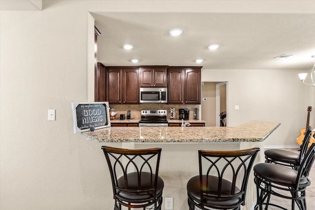 kitchen featuring a breakfast bar, an inviting chandelier, appliances with stainless steel finishes, dark brown cabinets, and light stone counters