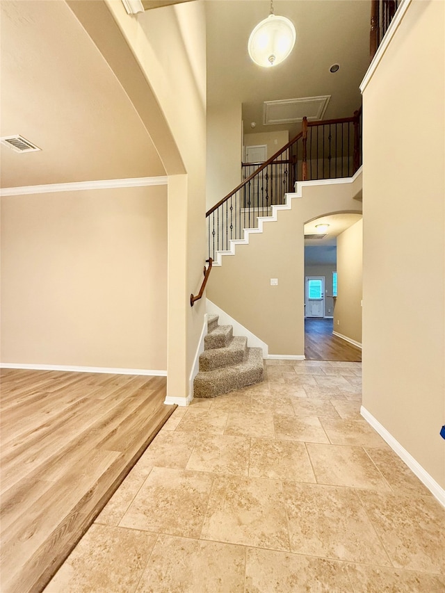 stairs featuring a towering ceiling, wood-type flooring, and ornamental molding