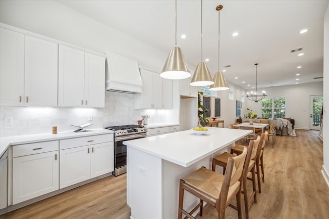 kitchen with custom exhaust hood, hanging light fixtures, stainless steel range oven, white cabinetry, and a breakfast bar area