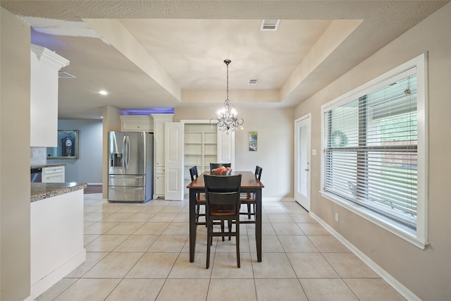 tiled dining space with a notable chandelier, a raised ceiling, and a textured ceiling