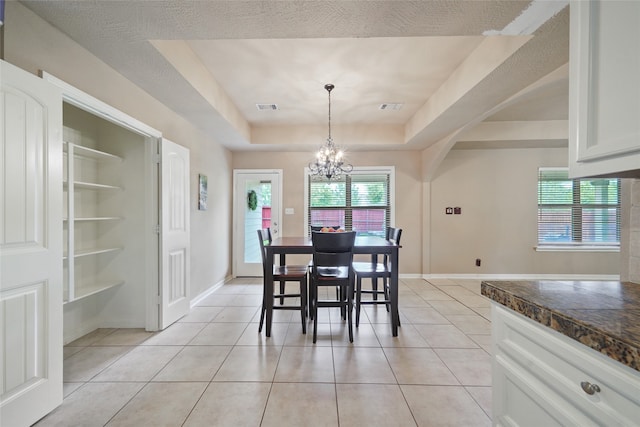 dining area with a textured ceiling, a tray ceiling, light tile patterned floors, and a notable chandelier