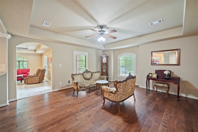 living room featuring a wealth of natural light, a tray ceiling, a textured ceiling, hardwood / wood-style floors, and ceiling fan