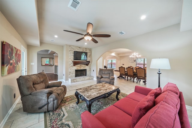 living room featuring ceiling fan with notable chandelier, light tile patterned floors, and a stone fireplace