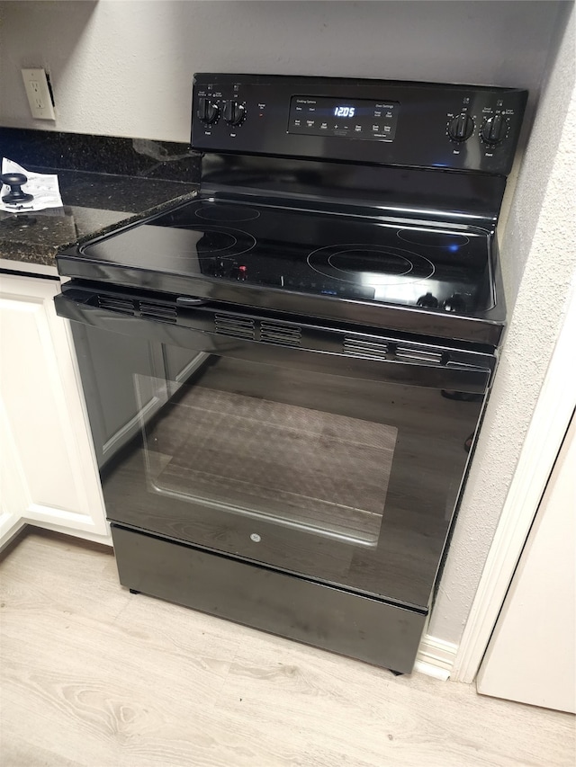 room details featuring light wood-type flooring, black / electric stove, dark stone countertops, and white cabinets