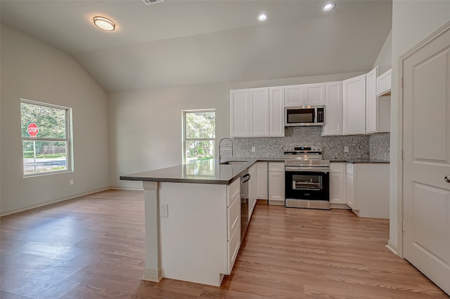 kitchen featuring sink, vaulted ceiling, kitchen peninsula, light hardwood / wood-style flooring, and appliances with stainless steel finishes