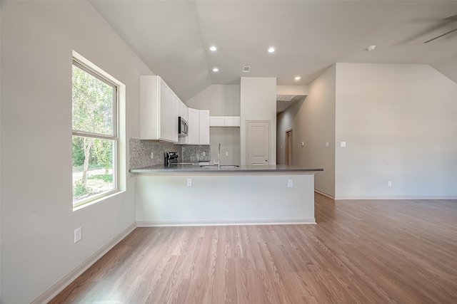 kitchen with light hardwood / wood-style floors, white cabinetry, vaulted ceiling, kitchen peninsula, and sink