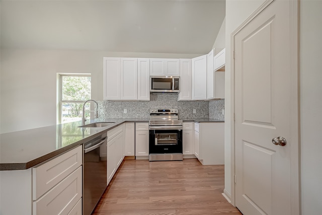 kitchen with sink, backsplash, white cabinetry, appliances with stainless steel finishes, and light hardwood / wood-style floors