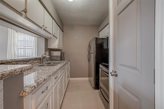 kitchen with light stone counters, white cabinets, light tile patterned floors, sink, and stainless steel appliances