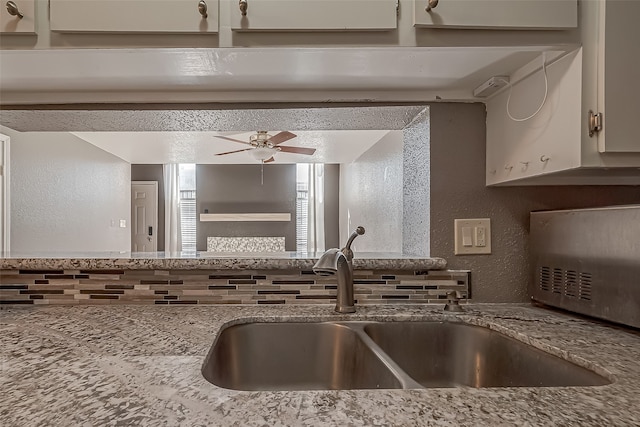 kitchen featuring white cabinets, tasteful backsplash, light stone countertops, ceiling fan, and sink