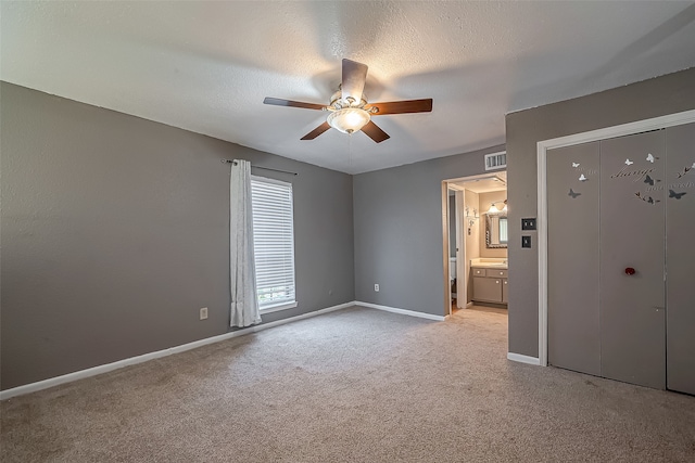 unfurnished bedroom with light carpet, ceiling fan, ensuite bathroom, and a textured ceiling