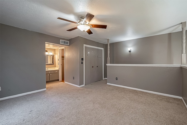 unfurnished bedroom featuring a closet, a textured ceiling, ceiling fan, ensuite bathroom, and light colored carpet