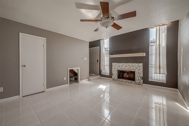 unfurnished living room with ceiling fan, light tile patterned flooring, a fireplace, and a textured ceiling