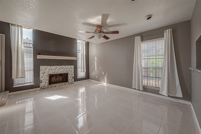 unfurnished living room featuring ceiling fan, a textured ceiling, a tiled fireplace, and light tile patterned flooring