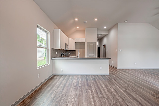 kitchen featuring light wood-type flooring, kitchen peninsula, white cabinetry, and vaulted ceiling