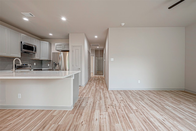 kitchen with light hardwood / wood-style floors, tasteful backsplash, kitchen peninsula, stainless steel appliances, and ceiling fan