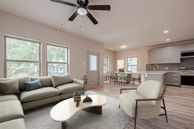 living room with light wood-type flooring, sink, and ceiling fan