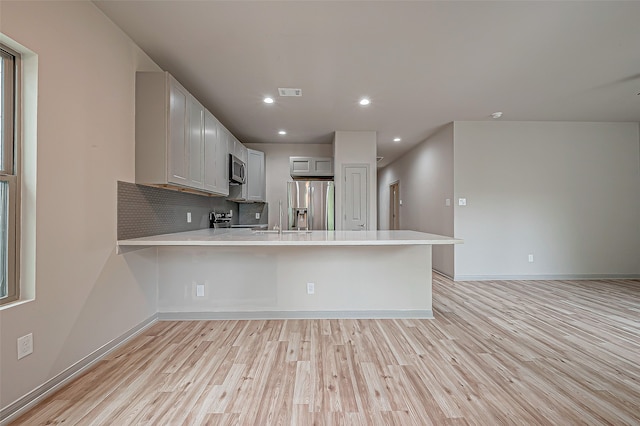 kitchen featuring light wood-type flooring, kitchen peninsula, and appliances with stainless steel finishes