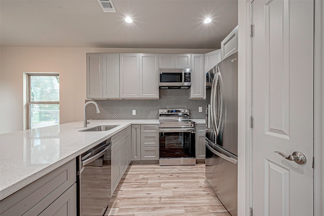 kitchen with light hardwood / wood-style floors, tasteful backsplash, light stone countertops, stainless steel appliances, and sink