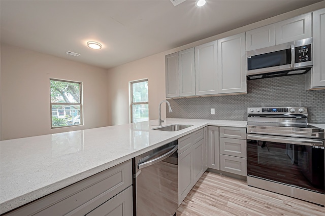 kitchen with sink, light hardwood / wood-style flooring, backsplash, stainless steel appliances, and light stone countertops