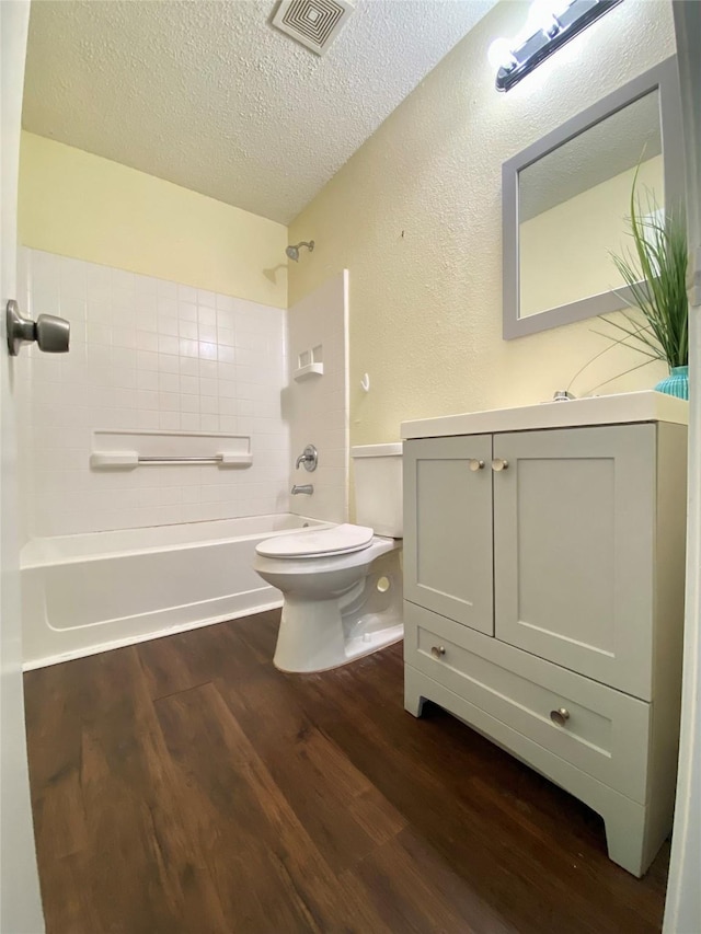 full bathroom with vanity, wood-type flooring, a textured ceiling, shower / bathtub combination, and toilet