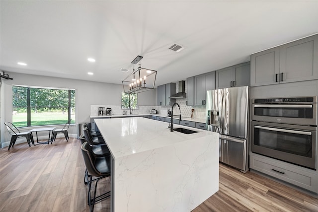 kitchen with light stone counters, stainless steel appliances, sink, a center island with sink, and light hardwood / wood-style floors