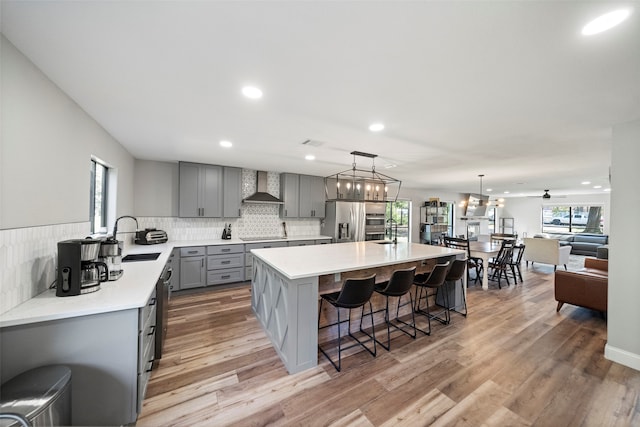 kitchen with gray cabinetry, wall chimney exhaust hood, stainless steel appliances, and light wood-type flooring