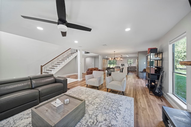 living room featuring ceiling fan with notable chandelier and light wood-type flooring