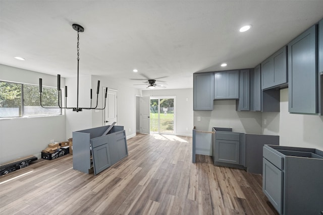 kitchen with gray cabinets, hanging light fixtures, ceiling fan with notable chandelier, and light wood-type flooring