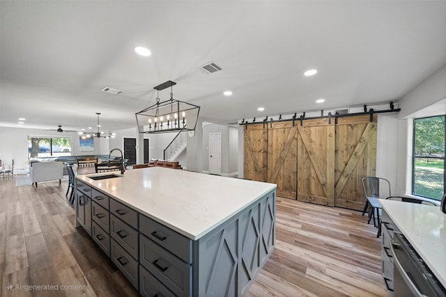 kitchen with light wood-type flooring, sink, a barn door, hanging light fixtures, and an island with sink