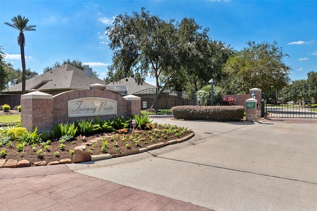 community / neighborhood sign featuring driveway, fence, and a gate