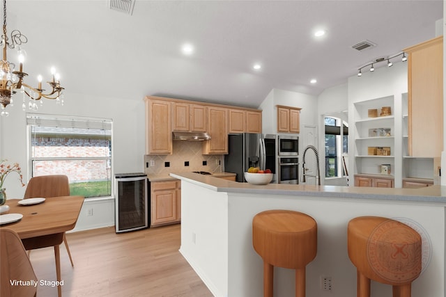 kitchen featuring pendant lighting, stainless steel appliances, light brown cabinets, beverage cooler, and under cabinet range hood