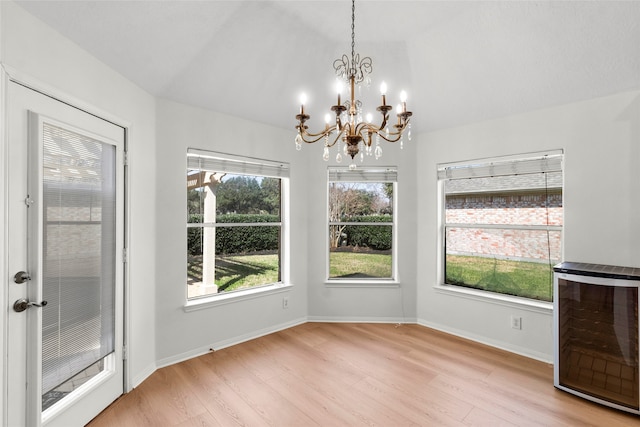 unfurnished dining area with wine cooler, baseboards, light wood finished floors, and an inviting chandelier