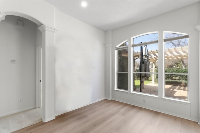 unfurnished dining area featuring arched walkways, baseboards, decorative columns, and light wood-style floors