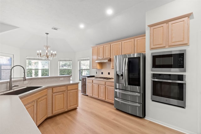 kitchen with stainless steel appliances, light countertops, hanging light fixtures, light brown cabinetry, and a sink