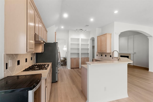 kitchen featuring light brown cabinets, under cabinet range hood, stainless steel gas cooktop, a peninsula, and light countertops