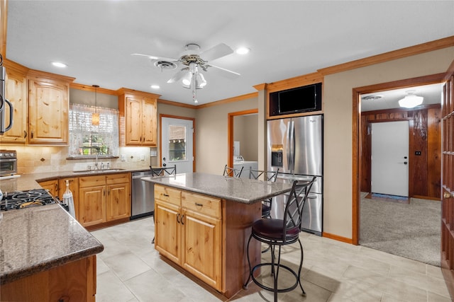 kitchen featuring washer and clothes dryer, a center island, sink, appliances with stainless steel finishes, and a kitchen bar