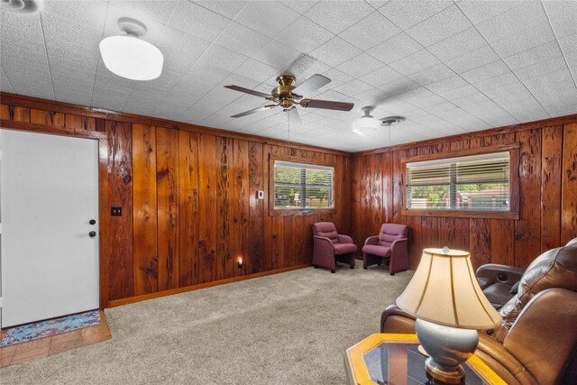 sitting room with carpet flooring, ornamental molding, ceiling fan, and wooden walls