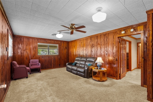 carpeted living room with ceiling fan, ornamental molding, and wood walls