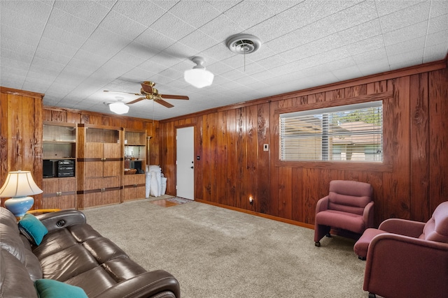 carpeted living room with wooden walls, ceiling fan, and ornamental molding