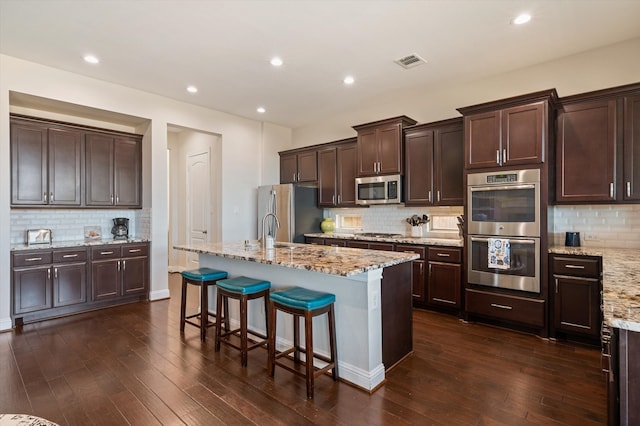 kitchen with an island with sink, stainless steel appliances, dark hardwood / wood-style floors, and tasteful backsplash