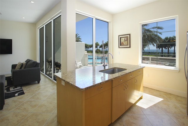 kitchen featuring light stone countertops, a center island with sink, light tile patterned floors, and sink