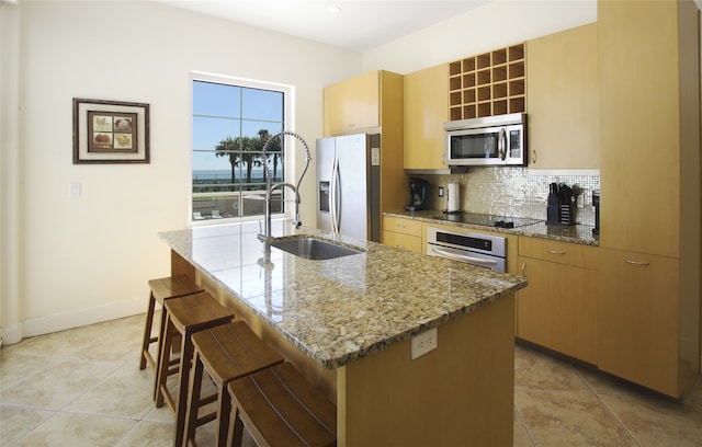 kitchen with backsplash, stone countertops, stainless steel appliances, a kitchen island with sink, and sink