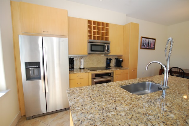 kitchen with tasteful backsplash, sink, stainless steel appliances, light stone countertops, and light brown cabinetry