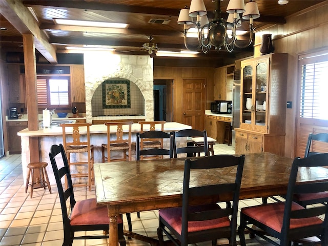 tiled dining area with wooden ceiling, ceiling fan with notable chandelier, wooden walls, and beamed ceiling