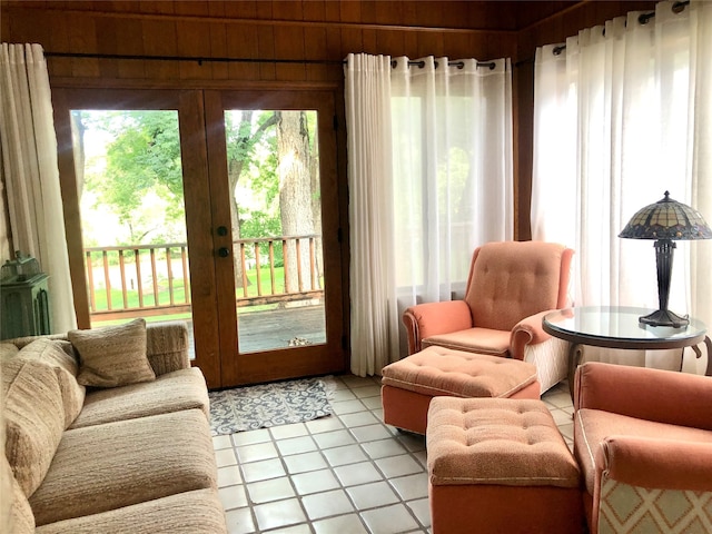 living room with french doors, wood walls, and light tile patterned floors