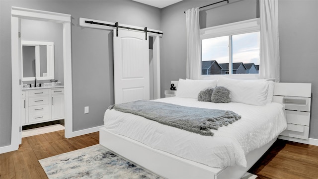 bedroom featuring sink, ensuite bath, hardwood / wood-style flooring, and a barn door