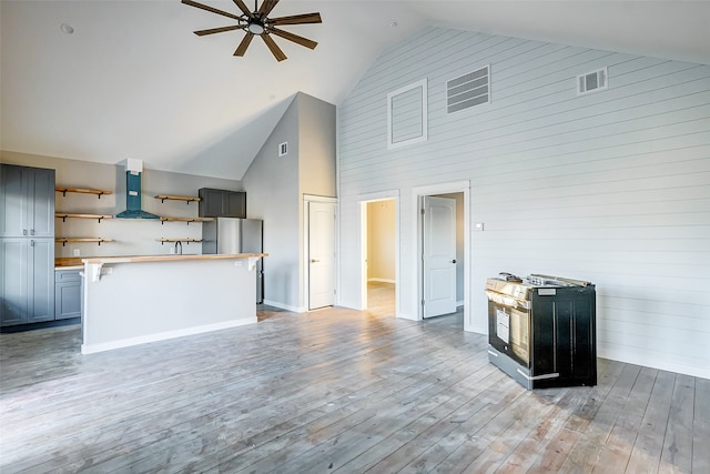 kitchen featuring wall chimney exhaust hood, light hardwood / wood-style floors, ceiling fan, and high vaulted ceiling