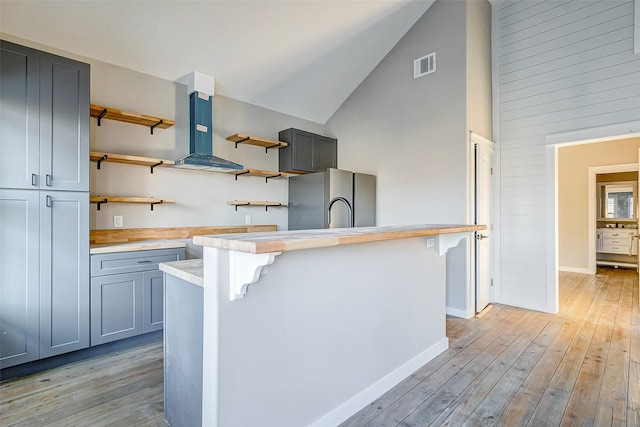 kitchen with stainless steel fridge, high vaulted ceiling, exhaust hood, a kitchen breakfast bar, and light hardwood / wood-style floors